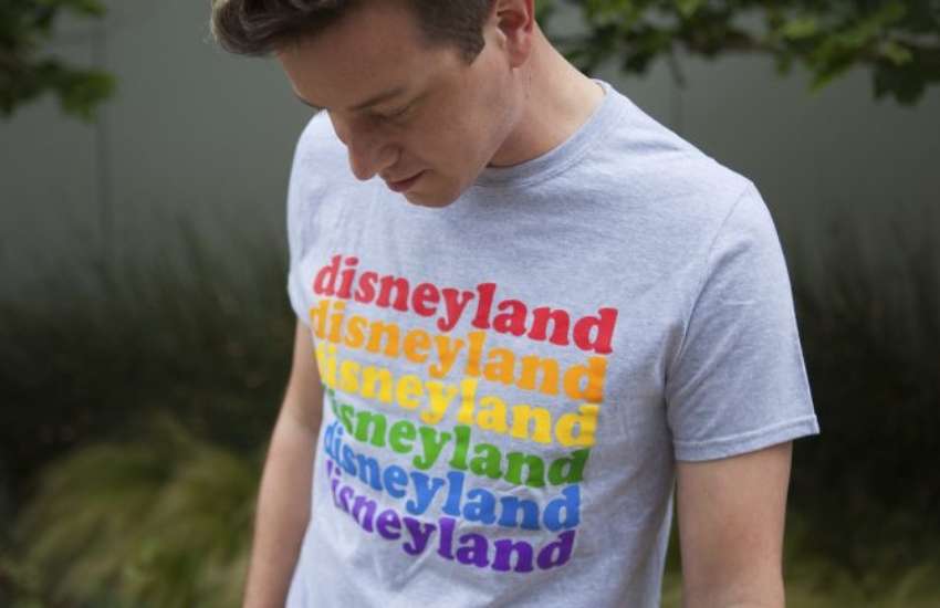 a man in a grey t-shirt he is looking down at and it has the word disneyland written over again in rainbow colours